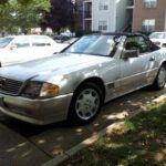 Front three quarter view of a silver 1995 Mercedes Benz SL500 parked outdoors, showcasing its classic roadster design and five-spoke wheels.