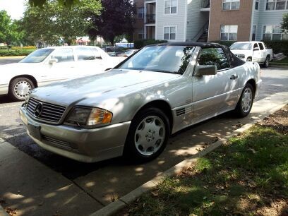 Front three quarter view of a silver 1995 Mercedes Benz SL500 parked outdoors, showcasing its classic roadster design and five-spoke wheels.