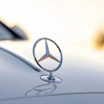 Close-Up Of Silver Mercedes-Benz Hood Ornament At Sunset