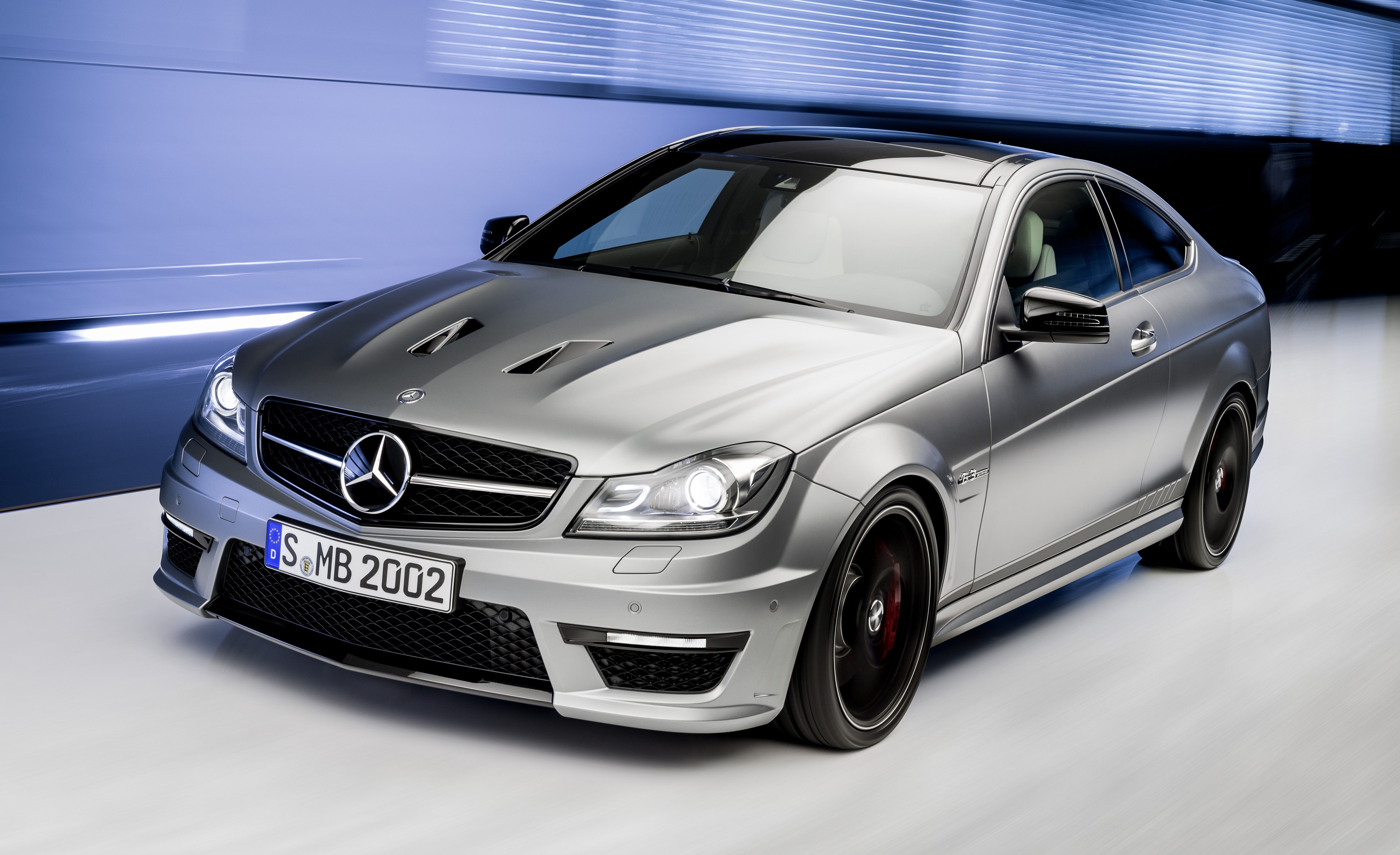 A gray 2013 Mercedes-Benz C63 AMG Coupe being driven dynamically, highlighting its sporty AMG styling and powerful performance capabilities.