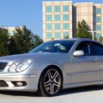 Front view of a silver Mercedes Benz AMG E55 W211, showcasing its powerful stance and headlight design, highlighting its value as a performance sedan.