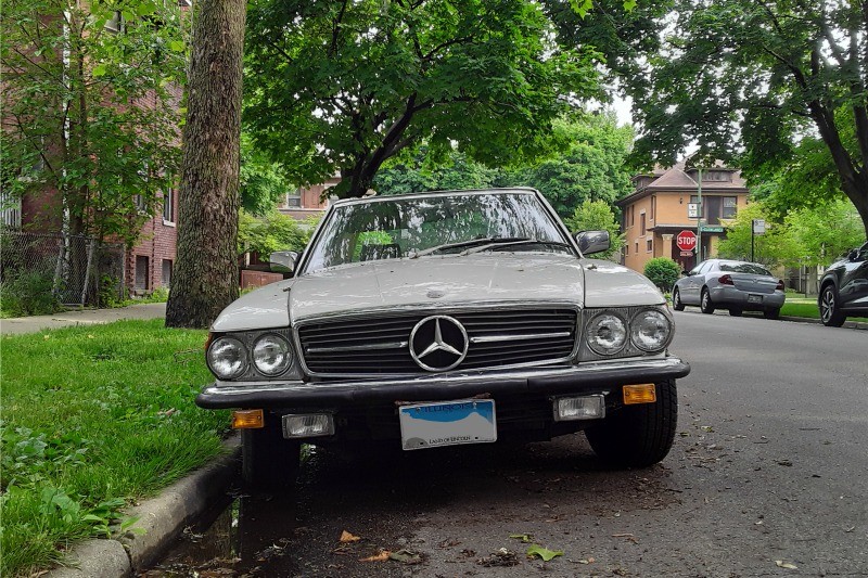 Front quarter view of a slightly worn 1981 Mercedes-Benz 380SL parked on a street, showcasing its classic roadster design