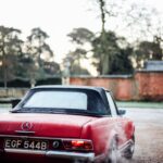 Front three quarter view of a red 1964 Benz 230 SL parked outdoors, showcasing its iconic Pagoda roof and classic design.