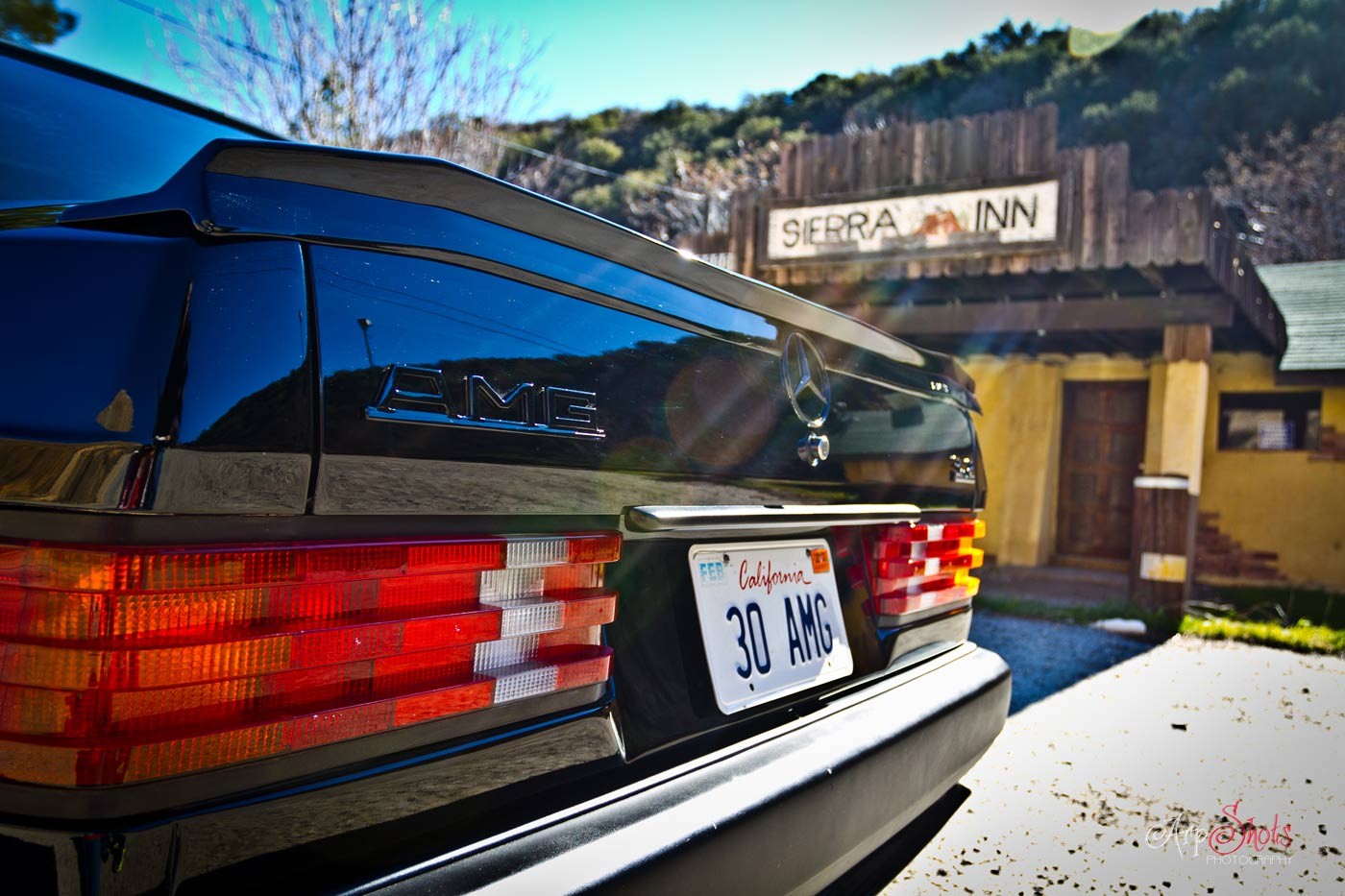 Front three quarter view of a silver Mercedes-Benz 190E 3.2 AMG Baby Hammer parked on a driveway, showcasing its AMG body kit and wheels.